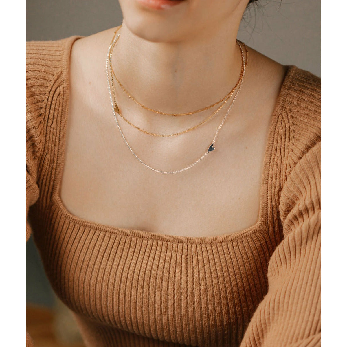 a women is wearing layered heart necklaces