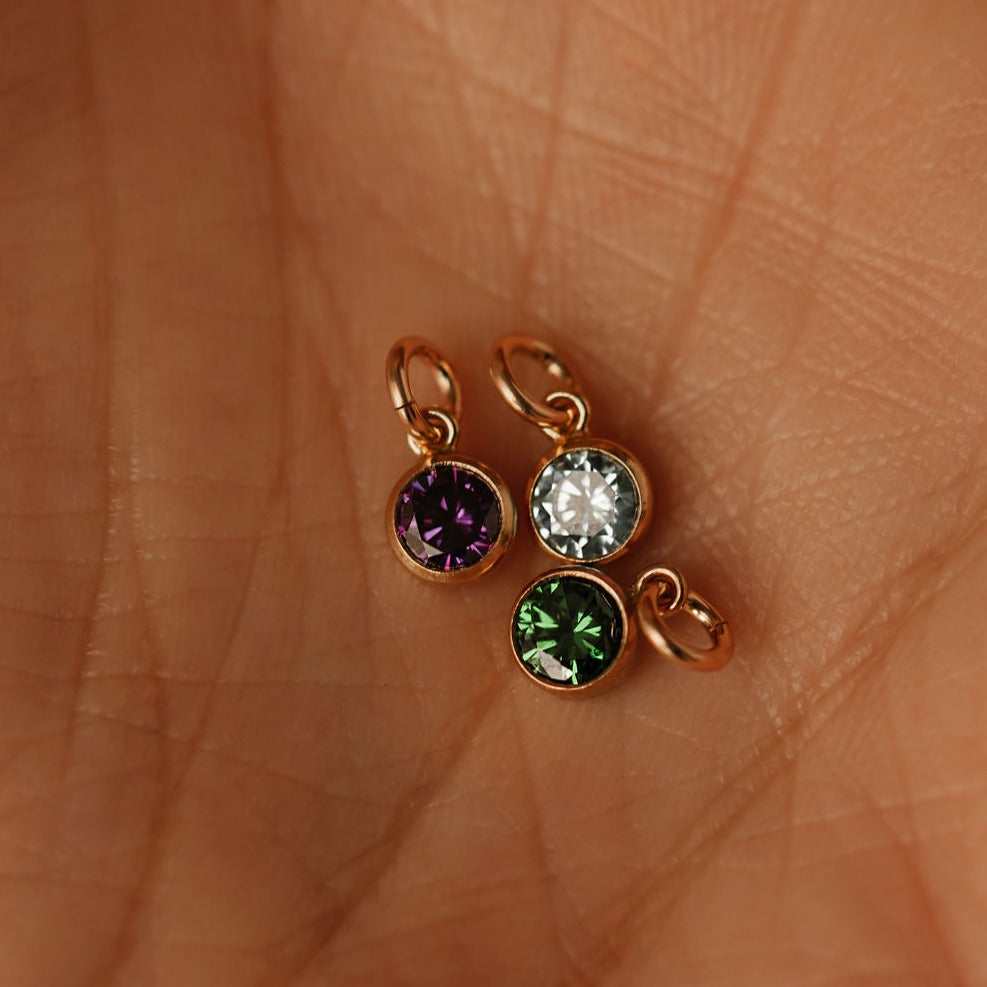 3 tiny birthstone gold charms are on the palm