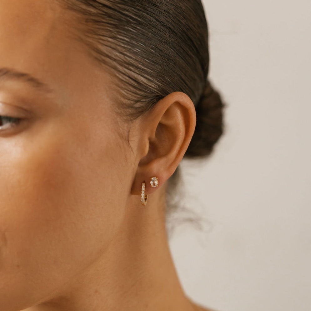 a woman is wearing pave diamond hoops with white topaz oval studs. 