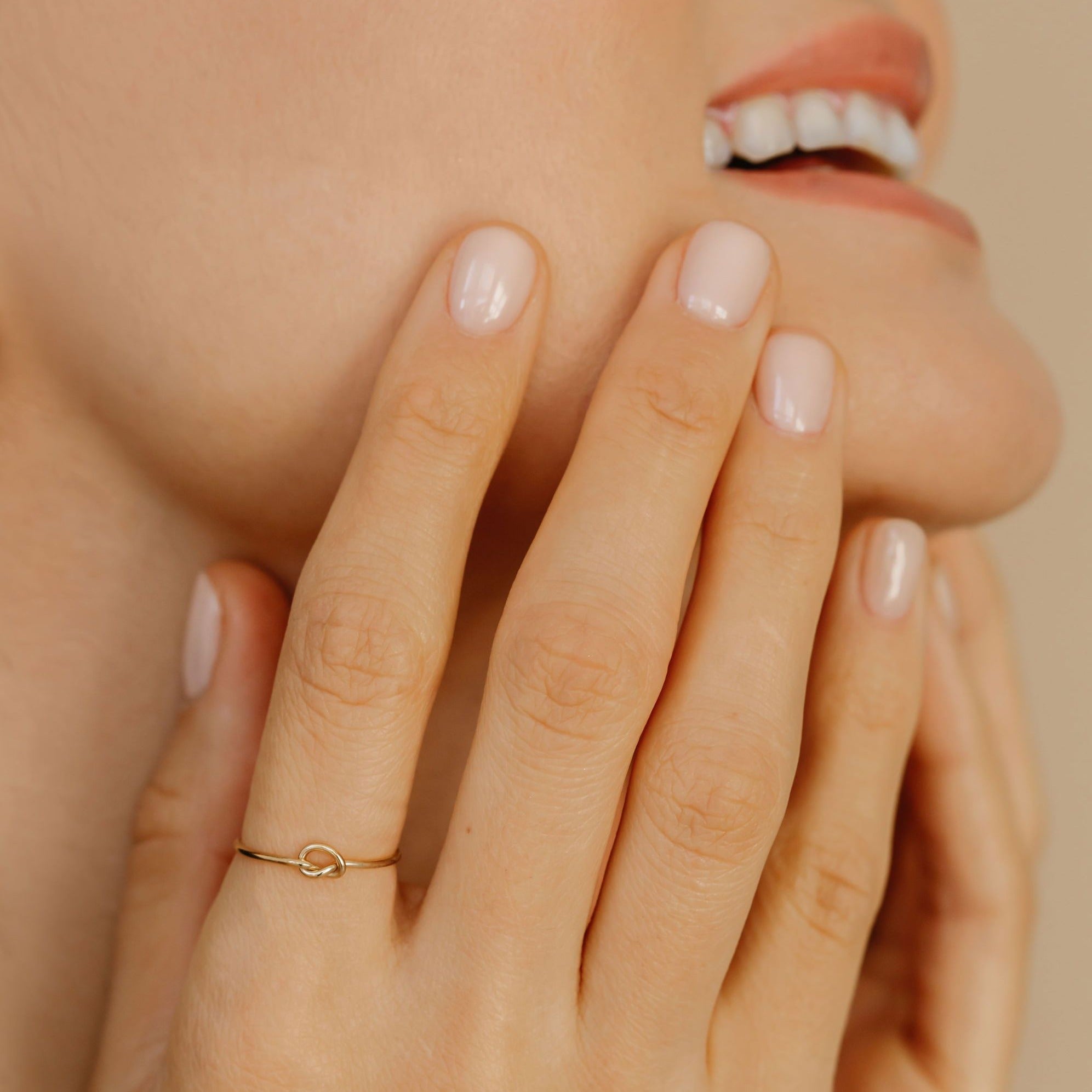 a woman  is smiling and wearing a dainty knot ring