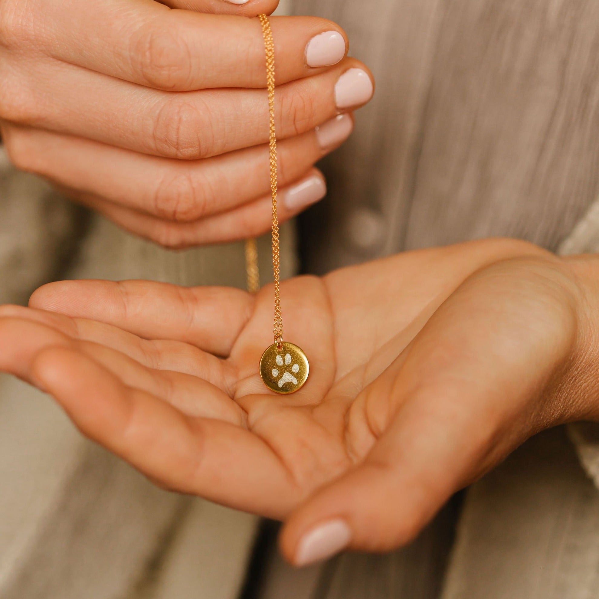 A women holding a paw print coin necklace made from actual pet prints