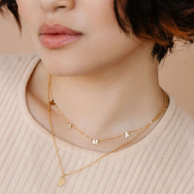 Model wearing a gold kid silhouette necklace layered with a gold necklace that spells out MAMA