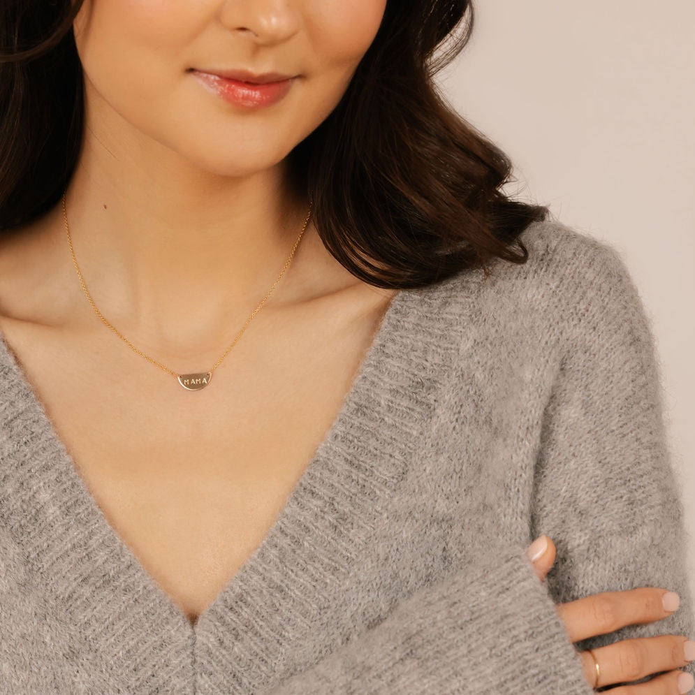 A woman is wearing a gold initial half moon disc necklace.